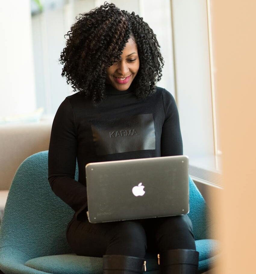 African American woman happily working on a laptop in a modern office setting.
