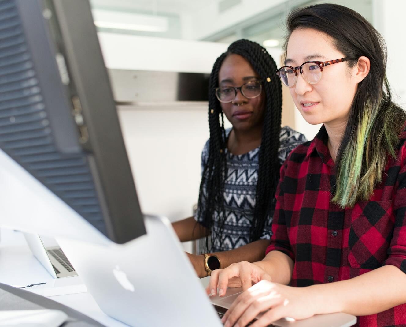 Two women working on a computer project together in an office setting.
